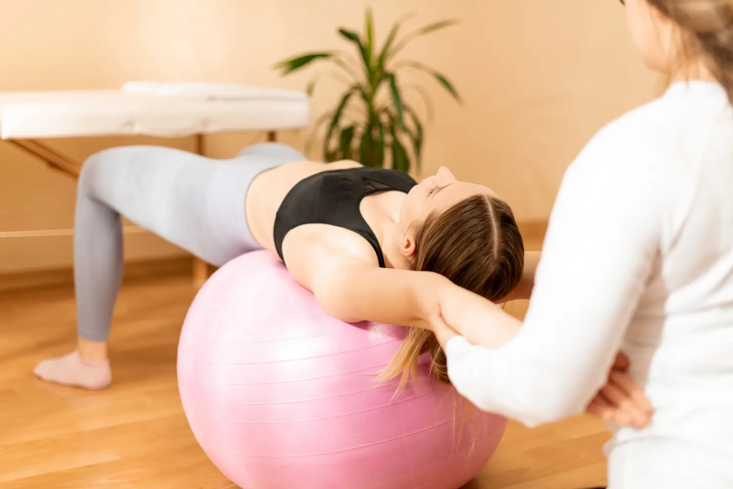 Agbalik Physiotherapie - Physiotherapeutin, die mit einer jungen Kundin mit Fitball an der Rumpfkraft arbeitet. Rehabilitation und physiotherapeutischer Hintergrund.